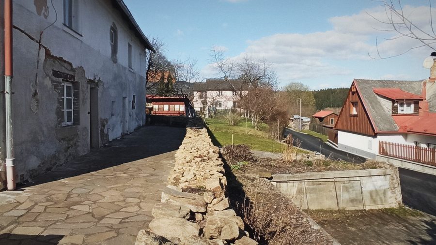 Kamenná dlažba podél domu, suchá zídka a výhled do vsi