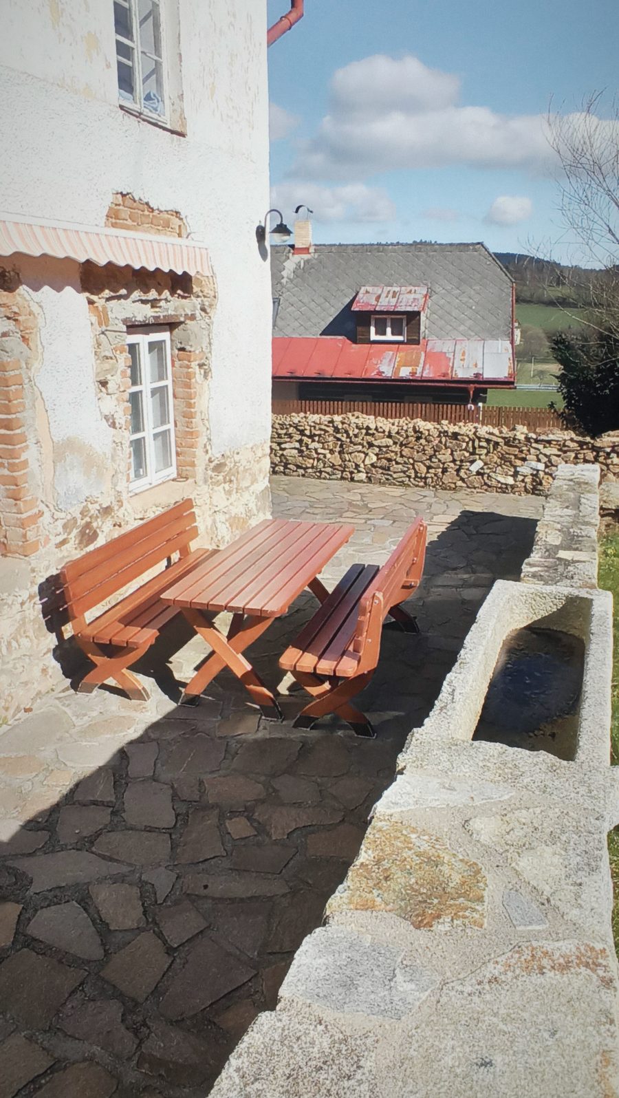 Dřevěný stůl s lavicemi na kamenné dlažbě u domu