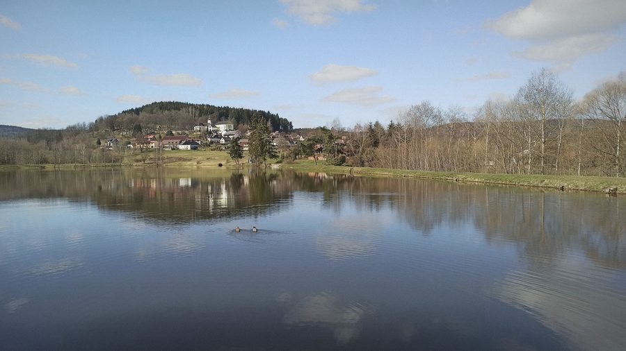 Rybník s odrazem oblohy, za ním vesnice na kopci